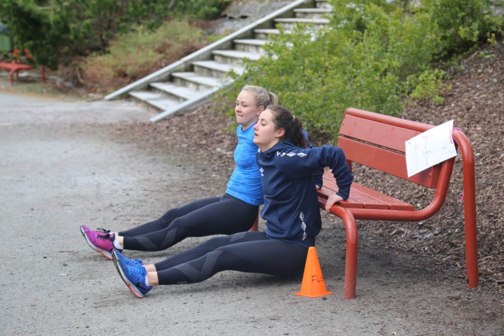 Helene Lian og Julie Belden Rasmussen trener armstyrke på en benk.